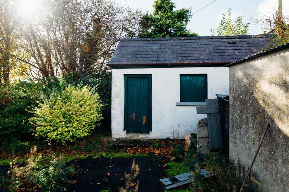 A quaint countryside shed basking in warm sunlight, surrounded by lush greenery and autumn leaves.